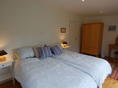 A bedroom with a double bed, two bedside tables with lamps, a wooden wardrobe, and a dressing table at Orchard Retreat in Sidmouth