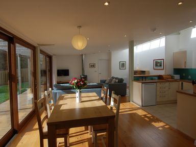 A dining table with chairs and a vase of flowers beside a living area with sofas and a wood burning stove at Orchard Retreat in Sidmouth