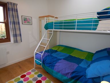 A bedroom with bunk beds with blue and green bedding a wooden floor a colorful polka dot rug and a window with blue plaid curtains at Orchard Retreat in Sidmouth