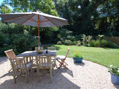An outdoor patio area with a wooden table and chairs under a large umbrella in a garden at Orchard Retreat in Sidmouth