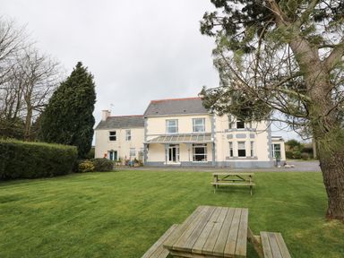 A large house with a covered porch and garden furniture on a lawn at Muriau Park in Caernarfon