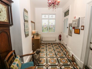 A hallway with patterned tiled floor a wooden chair a statue a dresser a lamp and stained glass window at Muriau Park in Caernarfon