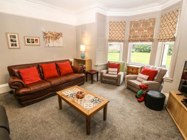 A living room with a brown leather sofa and red cushions two armchairs a wooden coffee table and patterned window blinds at Muriau Park in Caernarfon
