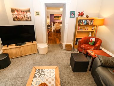 A living room with a television on a wooden stand a red armchair a black ottoman a wooden bookcase with books and decorations and a coffee table with patterned tiles at Muriau Park in Caernarfon