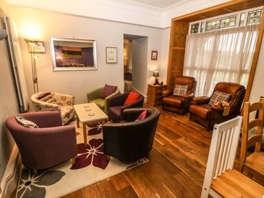 A sitting area with multiple armchairs around a small table and two leather chairs by a window at Muriau Park in Caernarfon