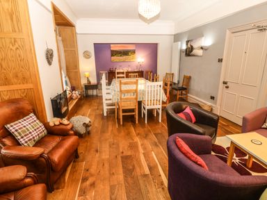 A dining room with a wooden table surrounded by mixed wooden and white chairs and a seating area with armchairs at Muriau Park in Caernarfon