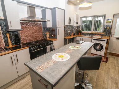 A kitchen with a stove oven unit a washing machine a kitchen island with a chair and countertop at Muriau Park in Caernarfon