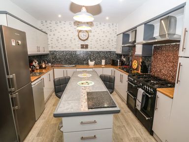 A kitchen with stainless steel refrigerator black stove and a kitchen island with chairs at Muriau Park in Caernarfon