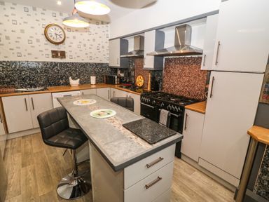A kitchen with an island and black bar stools a stove with two hoods cabinets countertops and a clock on the wall at Muriau Park in Caernarfon