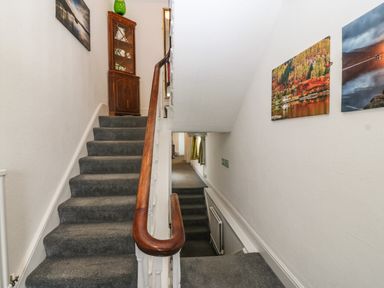 A stairway with gray carpet and wooden handrails with pictures on the wall at Muriau Park in Caernarfon