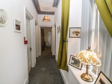 A hallway with closed doors carpeted floor pictures on the walls and a lamp on a window sill at Muriau Park in Caernarfon