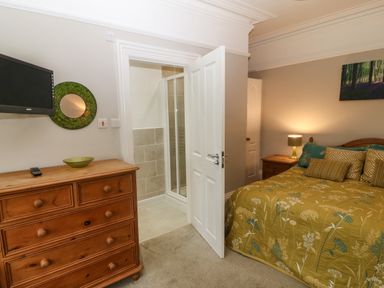 A bedroom with a bed covered in green patterned bedding next to a wooden dresser and a door leading to a shower room at Muriau Park in Caernarfon