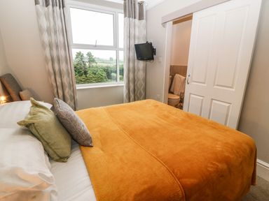 A bedroom with a bed covered with orange blanket two pillows and a window with curtains at Muriau Park in Caernarfon