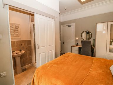 A bedroom with an orange bedspread a desk with a chair and mirror a wardrobe and an ensuite bathroom at Muriau Park in Caernarfon