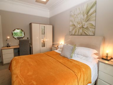 A bedroom with a bed covered with an orange blanket a wardrobe a desk with a chair and a round mirror at Muriau Park in Caernarfon
