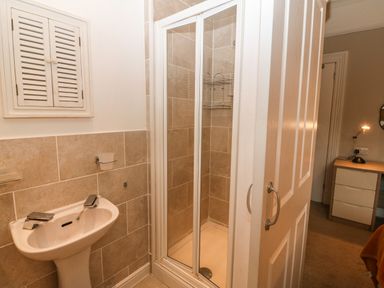 A bathroom with a pedestal sink and a tiled shower next to a door leading to a room with a desk at Muriau Park in Caernarfon