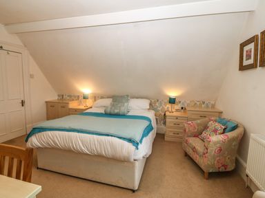 A bedroom with a double bed two bedside tables with lamps a floral armchair and a wooden chair at Muriau Park in Caernarfon