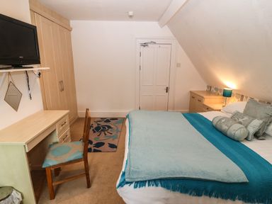 A bedroom with a bed with blue bedding a desk with a chair a wardrobe and a wall-mounted television at Muriau Park in Caernarfon