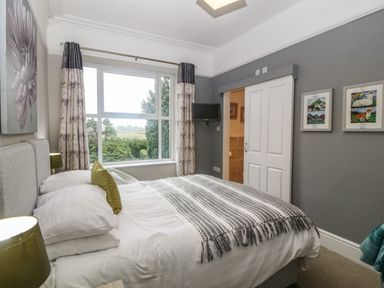 A bedroom with a bed a window with curtains and a wall mounted television at Muriau Park in Caernarfon