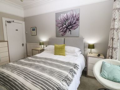 A bedroom with a bed a flower painting two bedside tables with lamps and a round chair at Muriau Park in Caernarfon