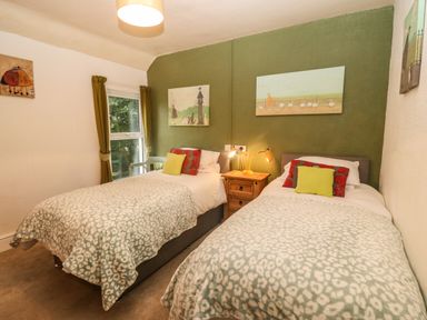 A bedroom with two single beds a wooden nightstand between them and green curtains at Muriau Park Caernarfon