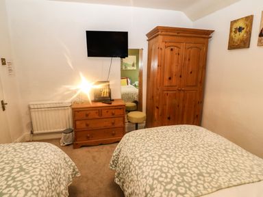A bedroom with two beds covered in patterned blankets a wooden chest of drawers with a lamp and mirror a wooden wardrobe and a wall-mounted television at Muriau Park in Caernarfon