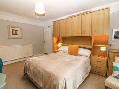 A bedroom with a double bed under wooden cabinets and bedside tables with lamps in Muriau Park in Caernarfon