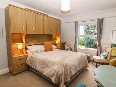 A bedroom with a double bed with overhead cabinets two chairs a window and a small table at Muriau Park in Caernarfon