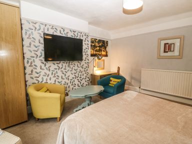 A bedroom with a bed a yellow and a blue armchair a small table a wall-mounted television and a desk at Muriau Park in Caernarfon