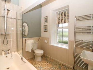 A bathroom with a bathtub shower combination a toilet a window with patterned blind and a wall-mounted towel radiator at Muriau Park in Caernarfon