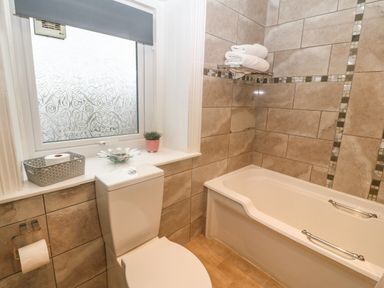 A bathroom with a toilet a bathtub with towels on a rack and a window with a blind at Muriau Park in Caernarfon