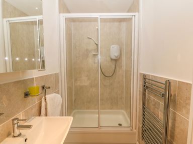 A bathroom with a sink and faucet a towel holder with a white towel a glass shelf with a yellow cup a mirror a shower enclosure with sliding glass doors and a showerhead a metal heated towel rail on the wall at Muriau Park in Caernarfon