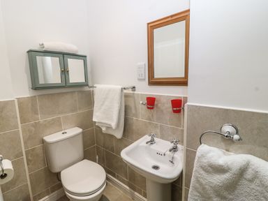 A small bathroom with a toilet, pedestal sink, mirror, wall cabinet, and towels at Muriau Park in Caernarfon