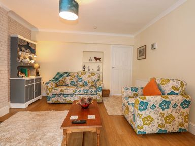 A living room with floral sofas a wooden coffee table a grey cabinet displaying china cups and a lamp at Muriau Park in Caernarfon