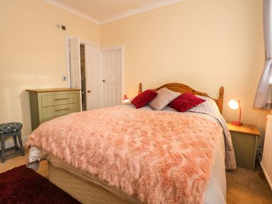 A bedroom with a bed covered with a pink fur blanket and pillows a green chest of drawers and a stool at Muriau Park in Caernarfon