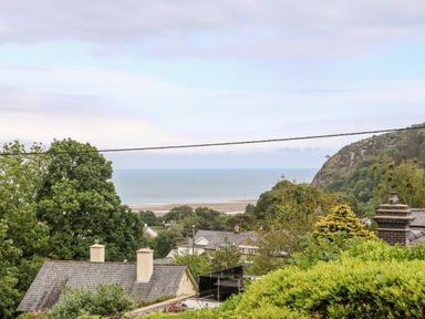 A view of houses and trees with the beach and sea in the background at 2 Argoed Llanbedrog