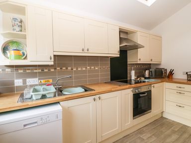 A kitchen with cream cabinets wood countertops a sink stove oven dishwasher and small appliances at 2 Argoed Llanbedrog