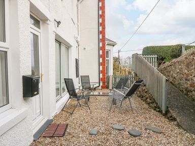 An outdoor seating area with four chairs and a glass table on a gravel ground next to a white building at 2 Argoed in Llanbedrog