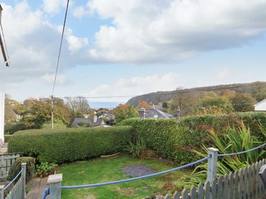 A garden with grass and hedges overlooking houses and hills at 2 Argoed in Llanbedrog