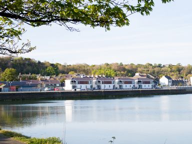 A row of houses along a waterfront with trees and hills in the background at 7 Marina View in Pwllheli