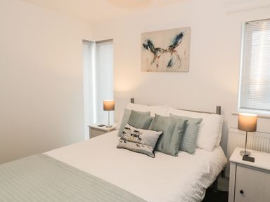 A bedroom with a double bed with pillows bedside tables with lamps and windows with blinds at 7 Marina View in Pwllheli