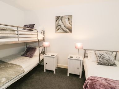 A bedroom with bunk beds single bed two nightstands with lamps and wall art at 7 Marina View in Pwllheli