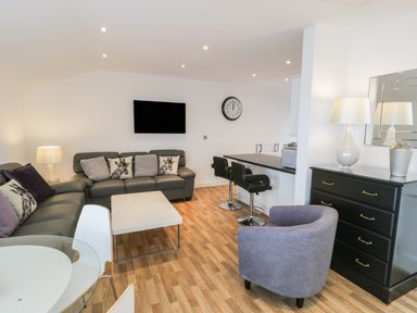 A living room with sofas pillows coffee table bar stools and a chest of drawers at 7 Marina View in Pwllheli