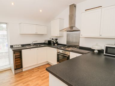 A kitchen with white cabinets black countertops a stainless steel oven gas stove and extractor fan a stainless steel sink a microwave and a wooden floor at 7 Marina View in Pwllheli
