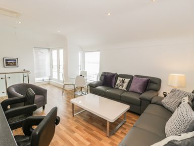 A living room with gray sofas white table and a round glass dining table with chairs at 7 Marina View in Pwllheli