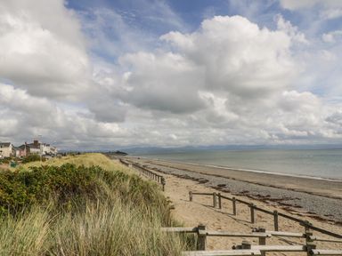 A sandy beach with wooden fence and grassy dunes beside houses under a cloudy sky at 7 Marina View in Pwllheli
