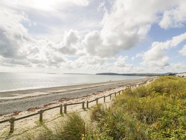 A beach with sand and pebbles next to grassy dunes and a wooden fence at 7 Marina View in Pwllheli