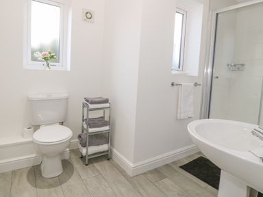 A bathroom with a toilet a sink a shower a towel rack with a towel and a small shelf with folded towels at 7 Marina View in Pwllheli