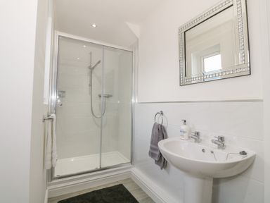 A bathroom with a glass shower enclosure a pedestal sink a mirror and towels at 7 Marina View in Pwllheli