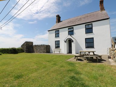 A white house with black windows a picnic table and bench on grass at Trefollwyn Mawr in Abersoch